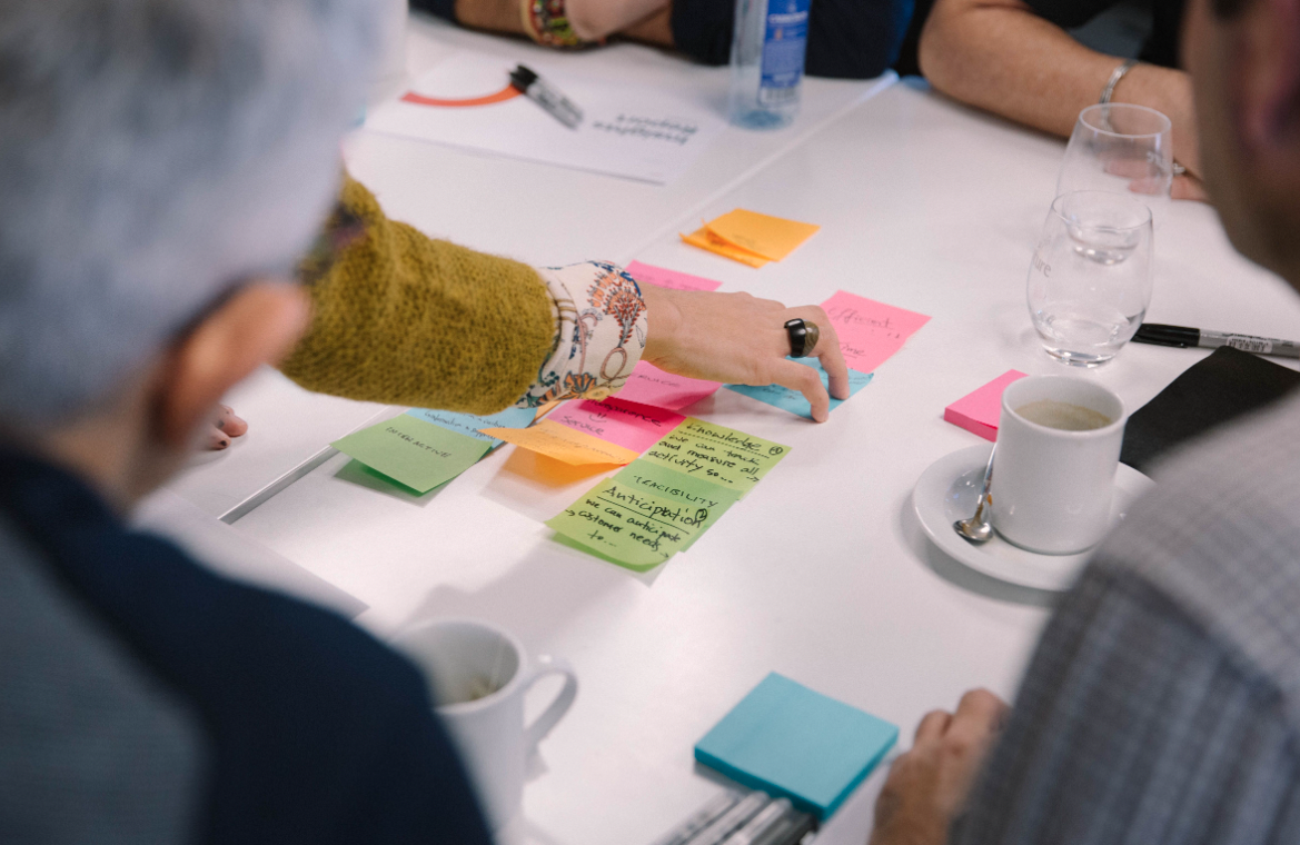 Workshop participants arranging colourful sticky notes on a table with coffee cups
